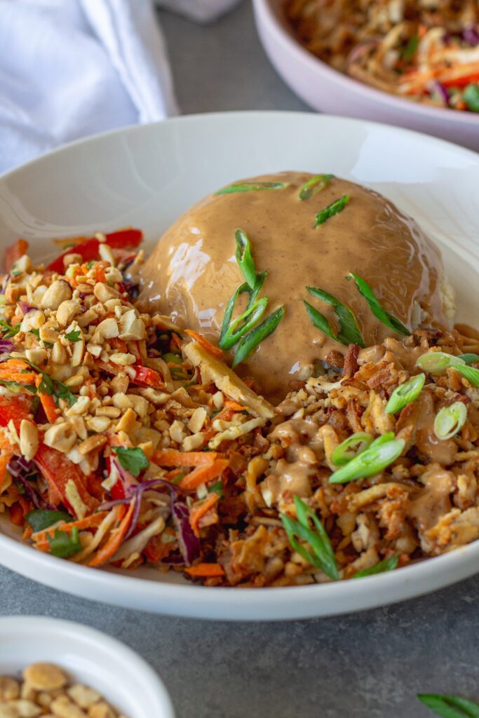 Bowl of crispy shredded tofu peanut bowls with creamy peanut sauce and colorful slaw, garnished with green onion and crushed peanuts.