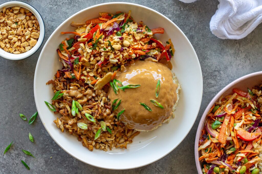 Bowl of crispy shredded tofu peanut bowls with creamy peanut sauce and colorful slaw, garnished with green onion and crushed peanuts.