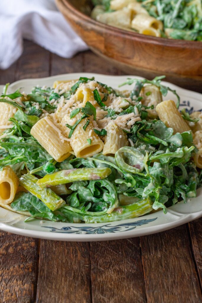 Close-up of finished Lemon Arugula Pasta Salad topped with vegan parmesan and fresh basil leaves.