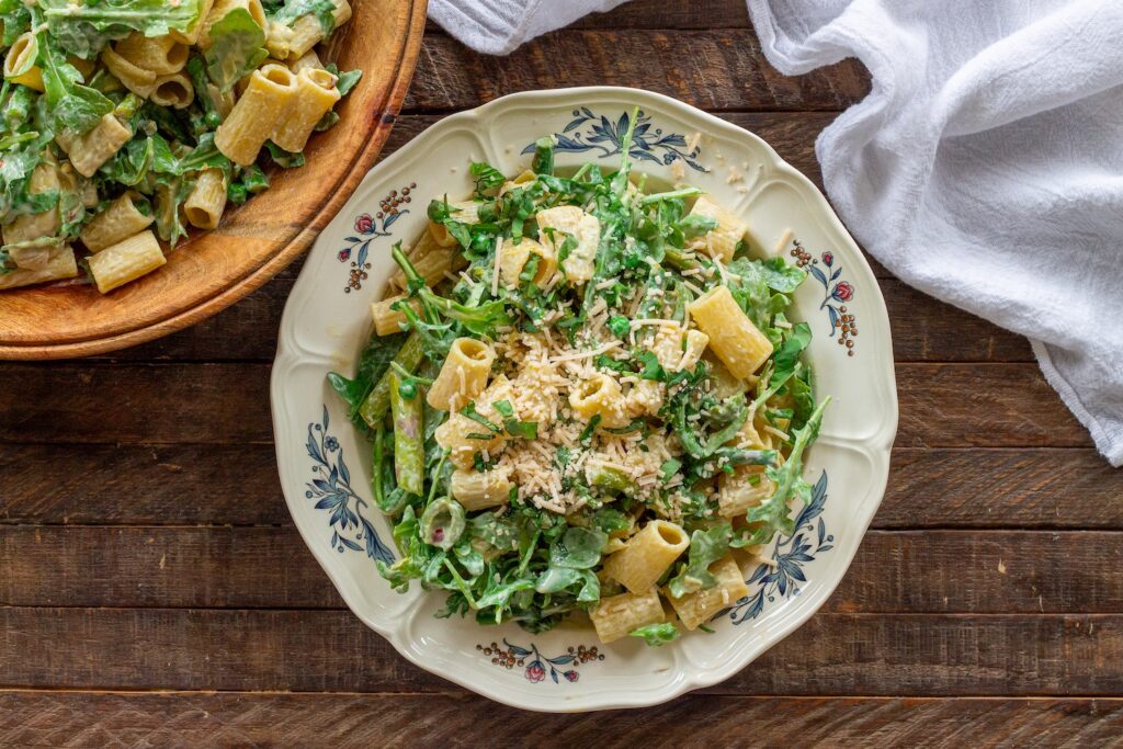 Close-up of finished Lemon Arugula Pasta Salad topped with vegan parmesan and fresh basil leaves.