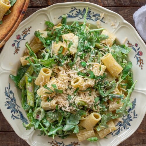 Close-up of finished Lemon Arugula Pasta Salad topped with vegan parmesan and fresh basil leaves.