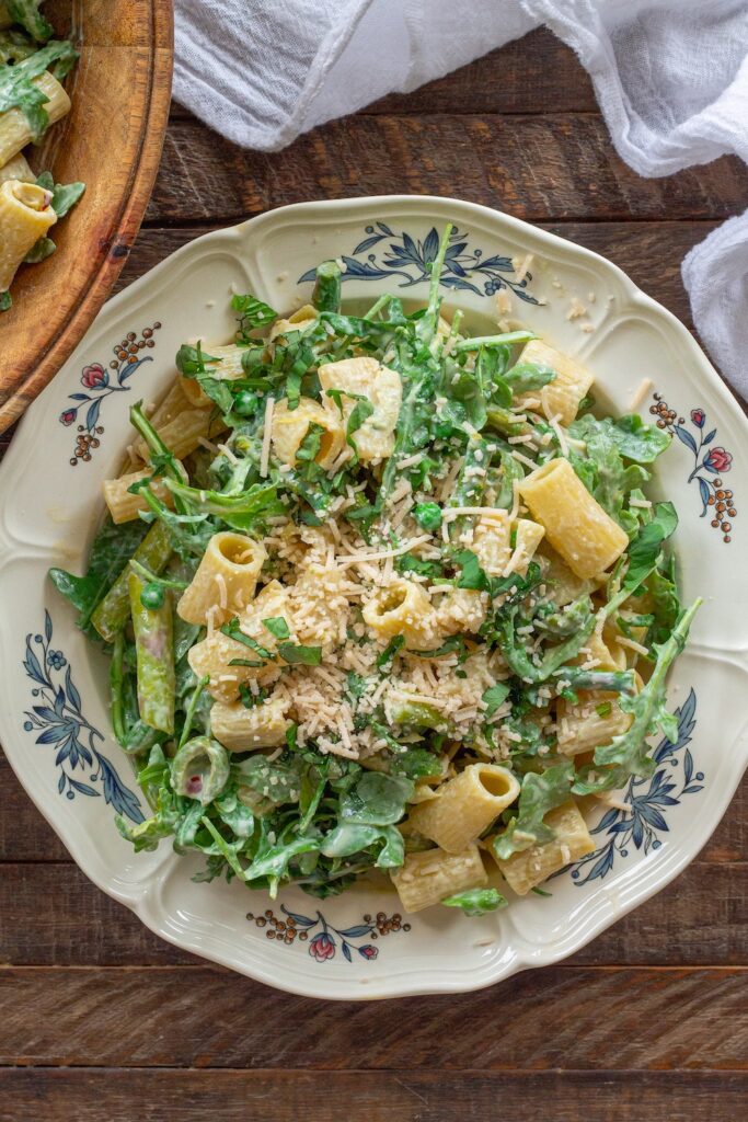 Close-up of finished Lemon Arugula Pasta Salad topped with vegan parmesan and fresh basil leaves.