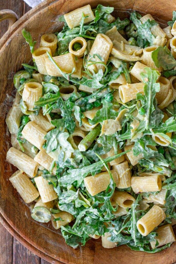 Close-up of finished Lemon Arugula Pasta Salad topped with vegan parmesan and fresh basil leaves.