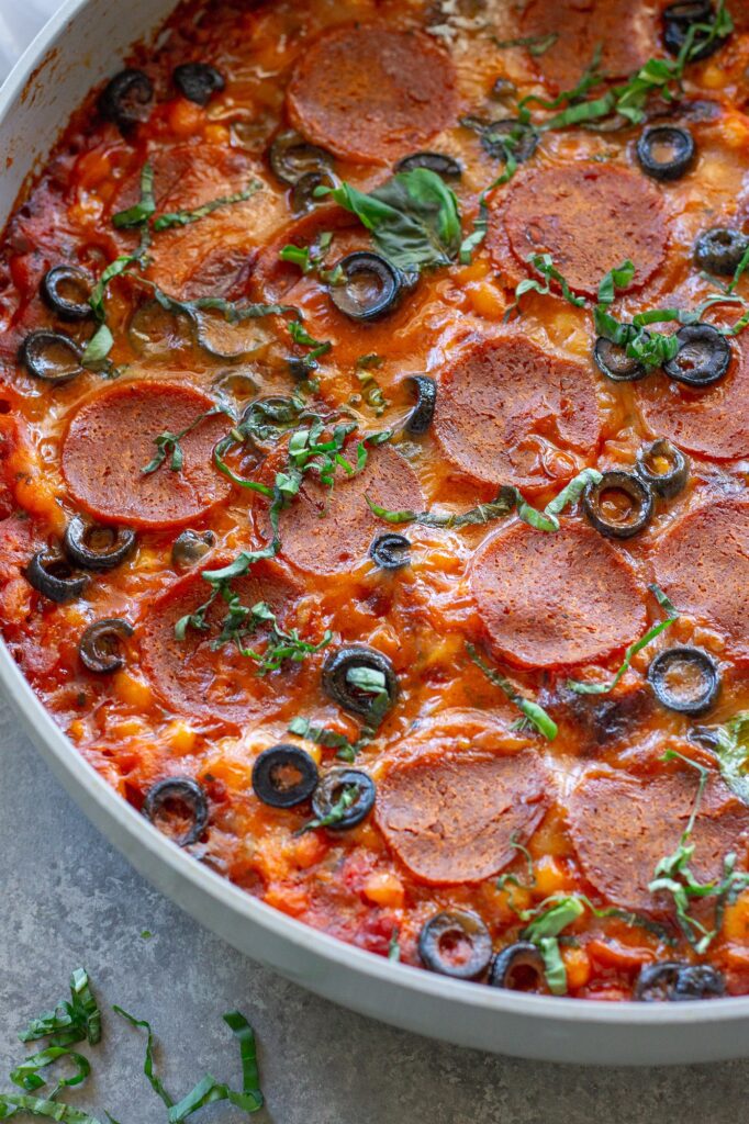 Vegan pizza beans in a skillet topped with melted vegan mozzarella, pepperoni, parmesan and fresh basil
