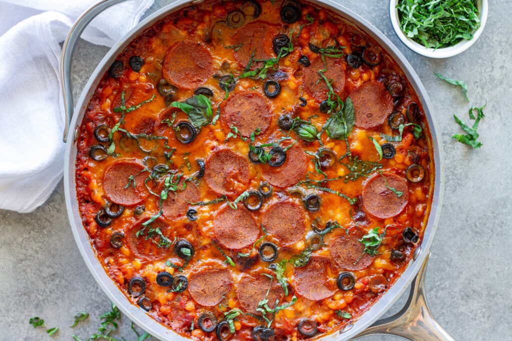 Vegan pizza beans in a skillet topped with melted vegan mozzarella, pepperoni, parmesan and fresh basil