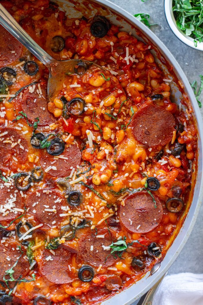 Vegan pizza beans in a skillet topped with melted vegan mozzarella, pepperoni, parmesan and fresh basil