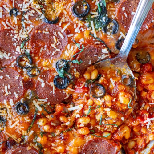 Vegan pizza beans in a skillet topped with melted vegan mozzarella, pepperoni, parmesan and fresh basil