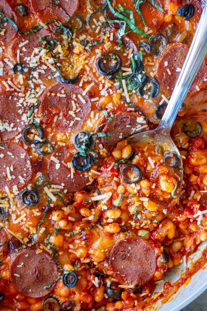 Vegan pizza beans in a skillet topped with melted vegan mozzarella, pepperoni, parmesan and fresh basil
