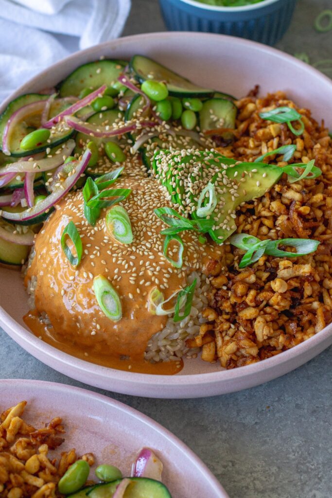 Vegan shredded tofu sushi bowl with sriracha sauce, cucumber edamame salad, avocado, and toasted sesame seeds
