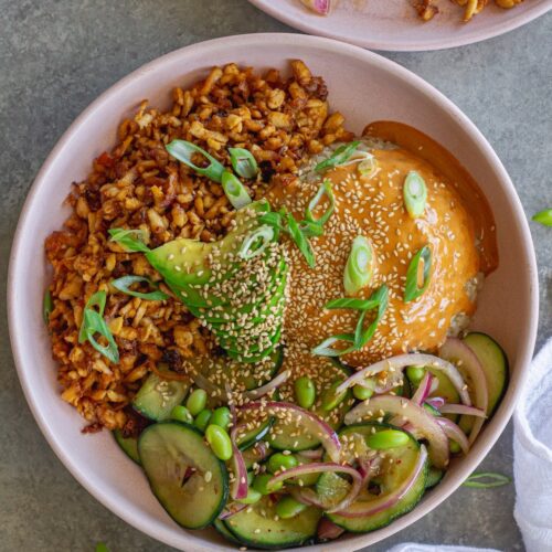 Vegan shredded tofu sushi bowl with sriracha sauce, cucumber edamame salad, avocado, and toasted sesame seeds