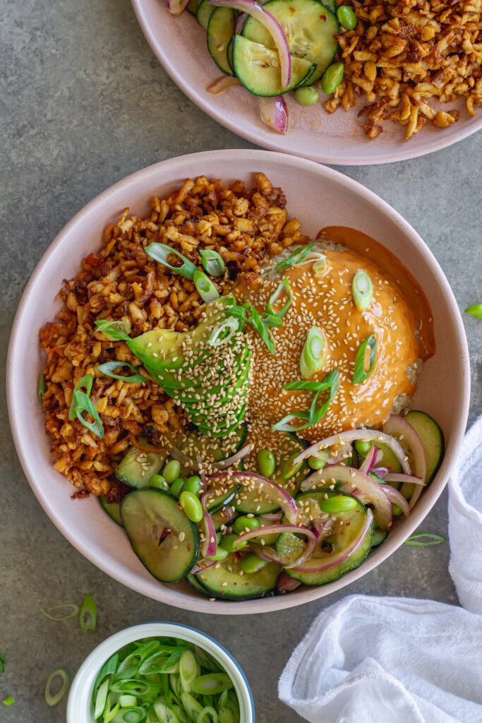 Vegan shredded tofu sushi bowl with sriracha sauce, cucumber edamame salad, avocado, and toasted sesame seeds