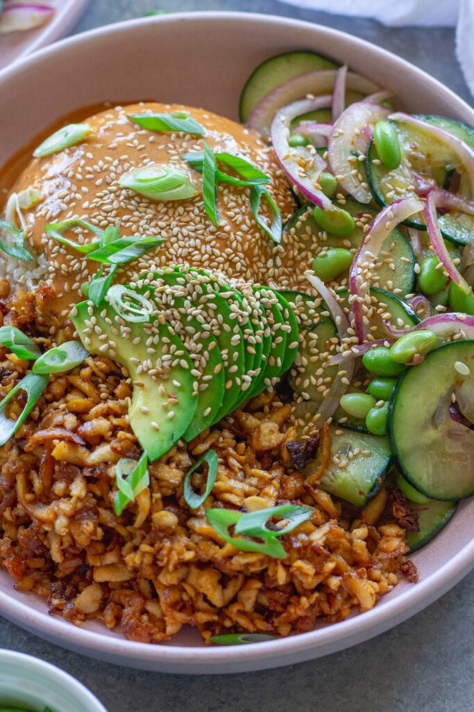 Vegan shredded tofu sushi bowl with sriracha sauce, cucumber edamame salad, avocado, and toasted sesame seeds