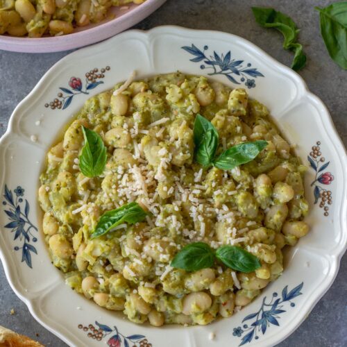 Creamy pea pesto white bean skillet on a serving plate garnished with fresh basil and vegan parmesan