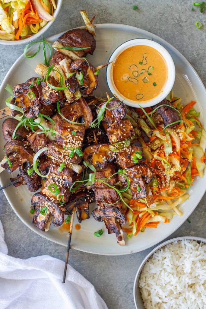Golden grilled Korean BBQ tofu skewers with mushrooms and scallions on bamboo skewers, served with a side of Gochujang mayonnaise and garnished with sesame seeds and green onions