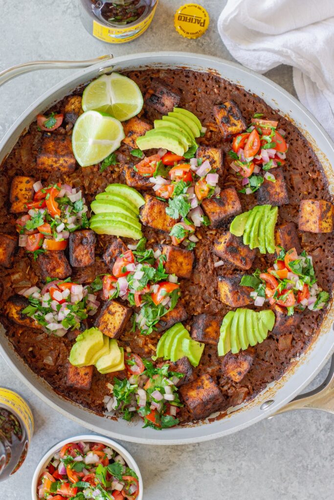 Close-up shot of one pan enchilada rice and crispy tofu cubes topped with pico de Gallo and fresh avocado slices.