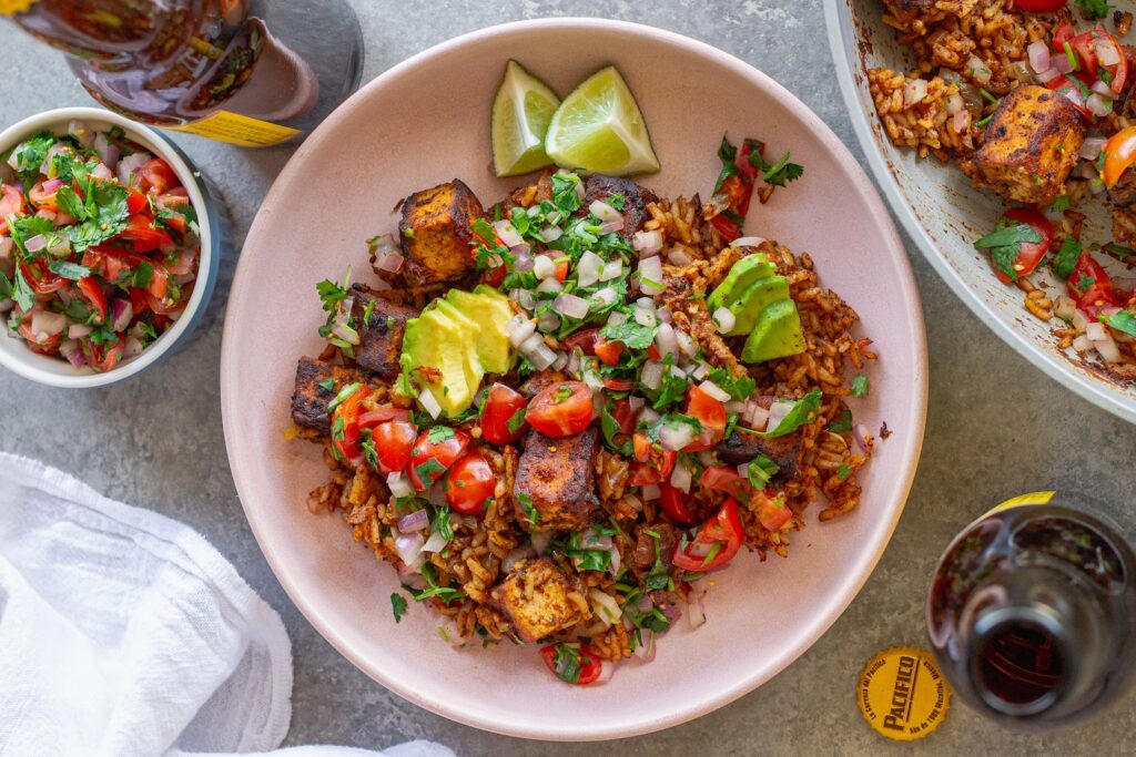 Close-up shot of one pan enchilada rice and crispy tofu cubes topped with pico de Gallo and fresh avocado slices.