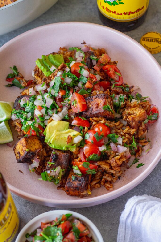 Close-up shot of one pan enchilada rice and crispy tofu cubes topped with pico de Gallo and fresh avocado slices.