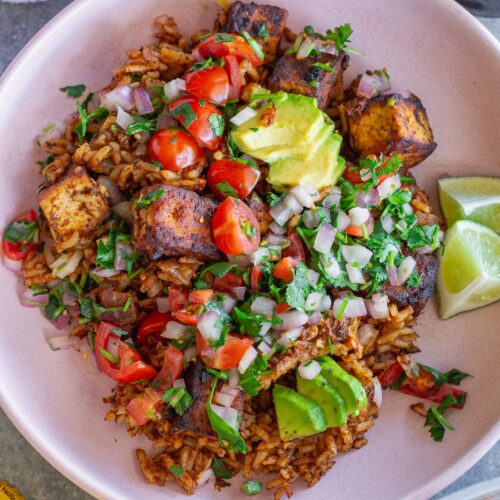 Close-up shot of one pan enchilada rice and crispy tofu cubes topped with pico de Gallo and fresh avocado slices.