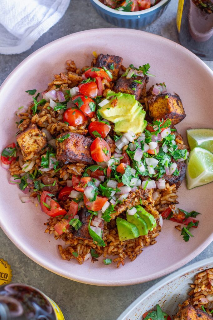 Close-up shot of one pan enchilada rice and crispy tofu cubes topped with pico de Gallo and fresh avocado slices.