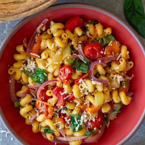 A colorful bowl of roasted sweet pepper pasta salad topped with fresh basil and vegan parmesan.
