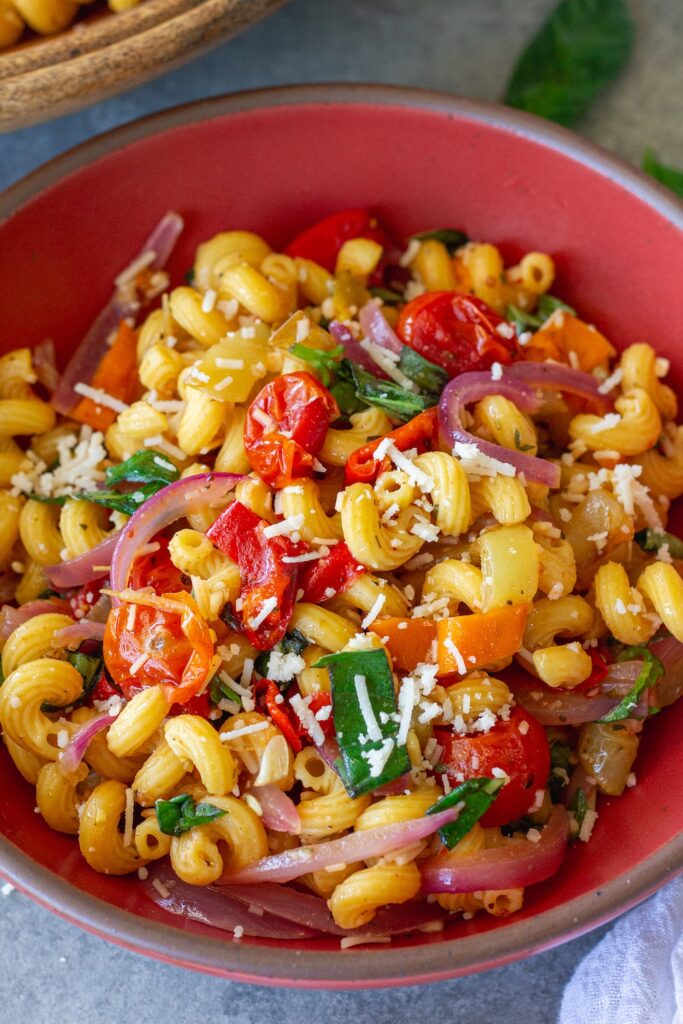 A colorful bowl of roasted sweet pepper pasta salad topped with fresh basil and vegan parmesan.