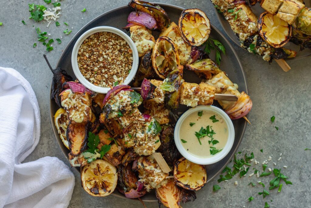 Close-up of grilled Tofu Caesar Kabobs, topped with creamy vegan caesar dressing, garlicky breadcrumbs and garnished with lemon wedges.