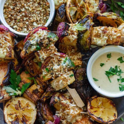 Close-up of grilled Tofu Caesar Kabobs, topped with creamy vegan caesar dressing, garlicky breadcrumbs and garnished with lemon wedges.