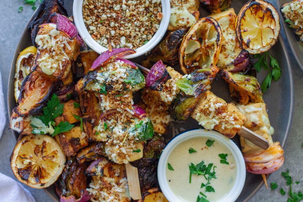 Close-up of grilled Tofu Caesar Kabobs, topped with creamy vegan caesar dressing, garlicky breadcrumbs and garnished with lemon wedges.