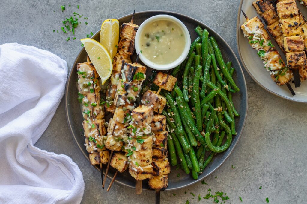 Golden grilled tofu piccata skewers drizzled with lemon-caper sauce, parmesan and parsley, and served with lemon wedges