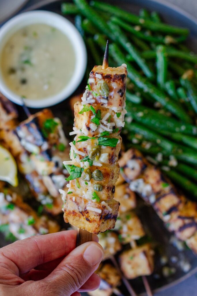 Golden grilled tofu piccata skewers drizzled with lemon-caper sauce, parmesan and parsley, and served with lemon wedges