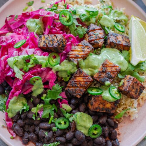 Vegan fish taco bowl with crispy blackened tofu, purple pickled cabbage, cilantro-lime rice, creamy avocado dressing, and garnished with fresh cilantro, jalapeño slices, and a lime wedge