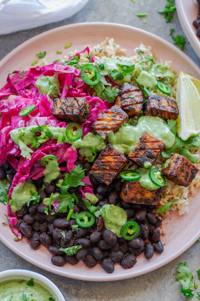 Vegan fish taco bowl with crispy blackened tofu, purple pickled cabbage, cilantro-lime rice, creamy avocado dressing, and garnished with fresh cilantro, jalapeño slices, and a lime wedge