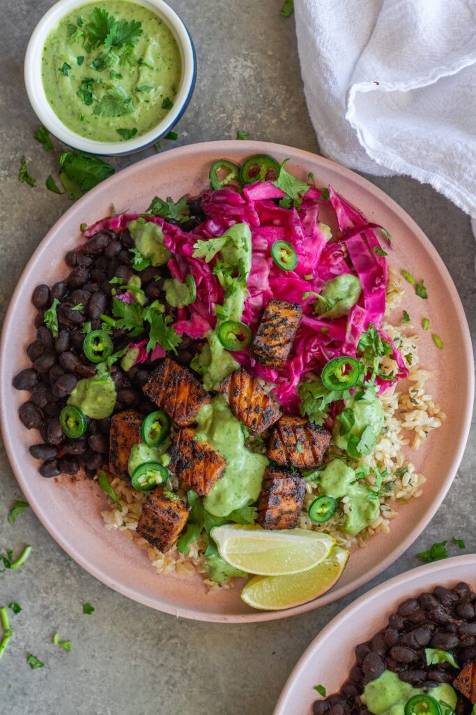 Vegan fish taco bowl with crispy blackened tofu, purple pickled cabbage, cilantro-lime rice, creamy avocado dressing, and garnished with fresh cilantro, jalapeño slices, and a lime wedge