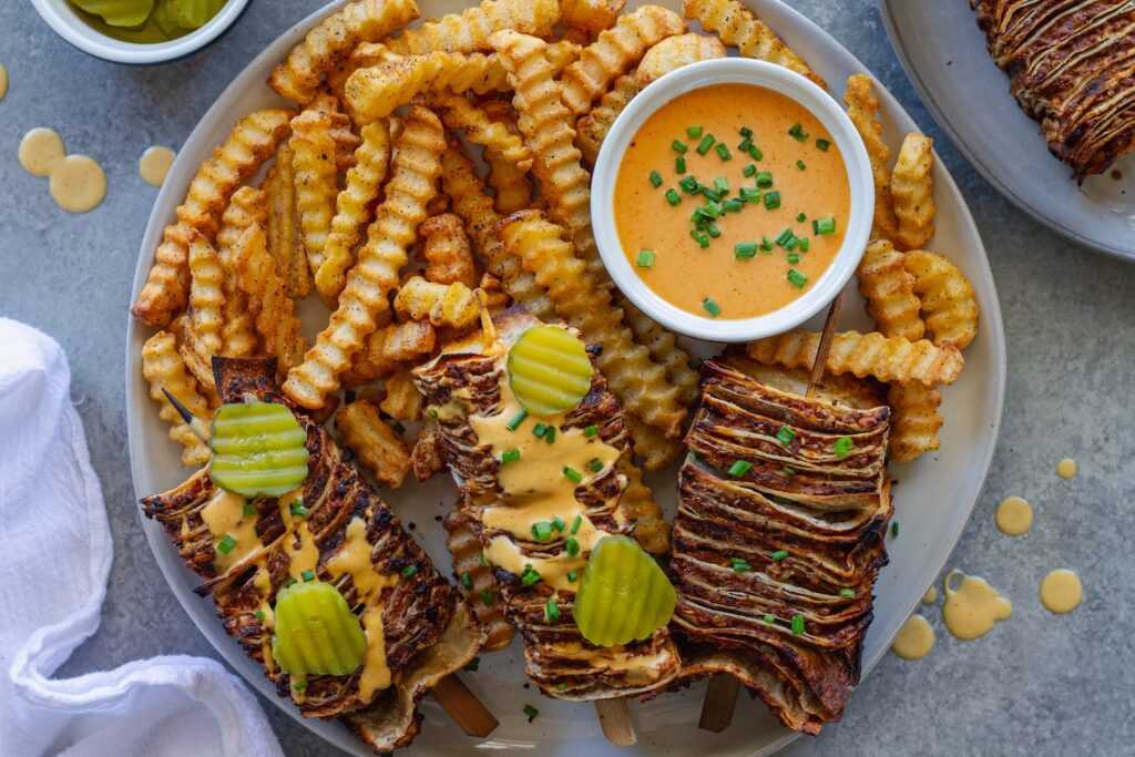 Golden brown vegan cheeseburger tortilla kabobs on wooden skewers with burger sauce drizzle and fresh dill pickles