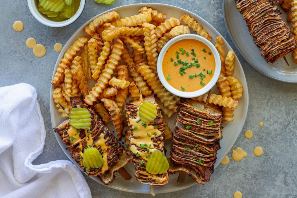 Golden brown vegan cheeseburger tortilla kabobs on wooden skewers with burger sauce drizzle and fresh dill pickles