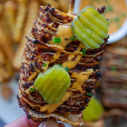 Golden brown vegan cheeseburger tortilla kabobs on wooden skewers with burger sauce drizzle and fresh dill pickles