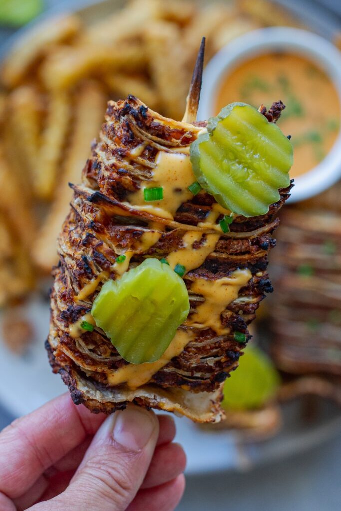 Golden brown vegan cheeseburger tortilla kabobs on wooden skewers with burger sauce drizzle and fresh dill pickles