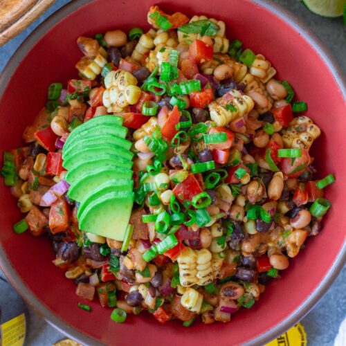 A bowl of colorful cowboy caviar with black beans, corn, diced tomatoes, red bell pepper, and black-eyed peas tossed in a smoky chipotle-lime dressing, garnished with fresh cilantro, served with tortilla chips on the side.