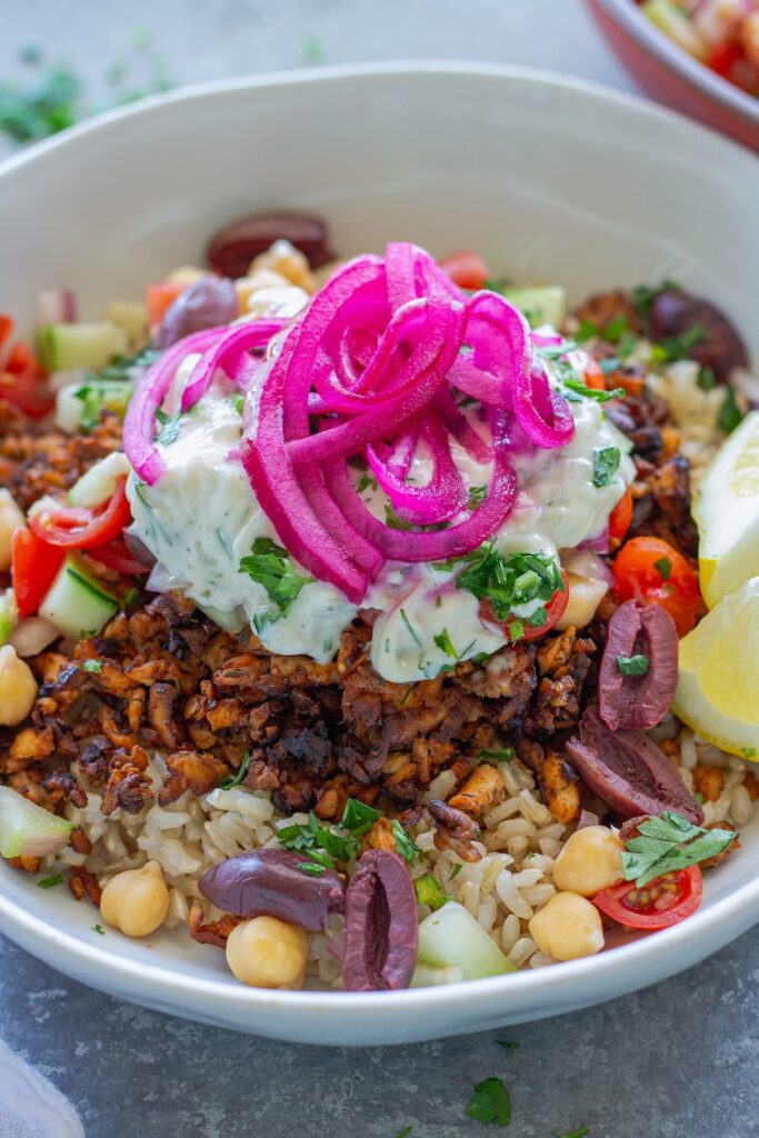Mediterranean-inspired tofu bowl with crispy seasoned tofu, chickpea salad, rice, Kalamata olives, vegan tzatziki and pickled red onions
