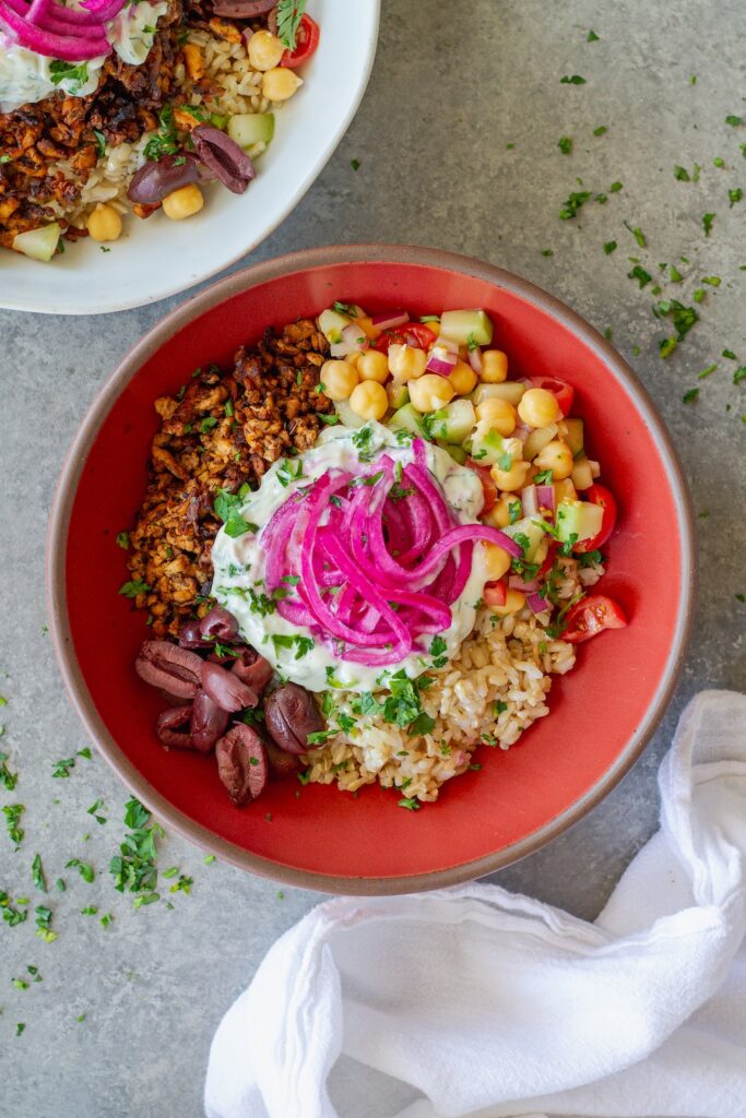 Mediterranean-inspired tofu bowl with crispy seasoned tofu, chickpea salad, rice, Kalamata olives, vegan tzatziki and pickled red onions