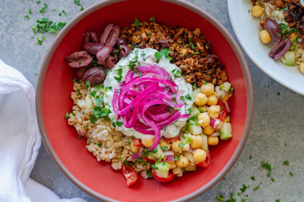 Mediterranean-inspired tofu bowl with crispy seasoned tofu, chickpea salad, rice, Kalamata olives, vegan tzatziki and pickled red onions