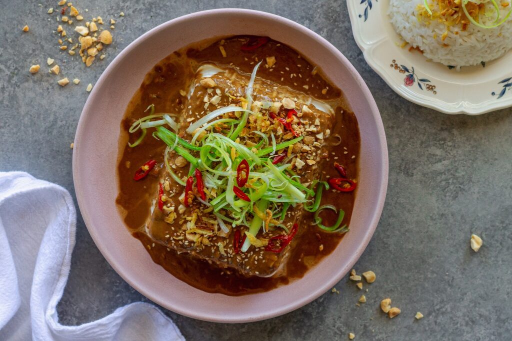Silken tofu with spicy sesame sauce, topped with green onions, sesame seeds, and crushed peanuts