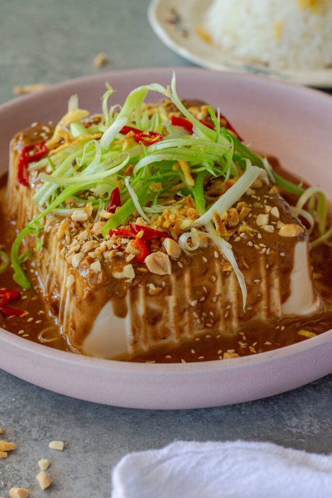 Silken tofu with spicy sesame sauce, topped with green onions, sesame seeds, and crushed peanuts