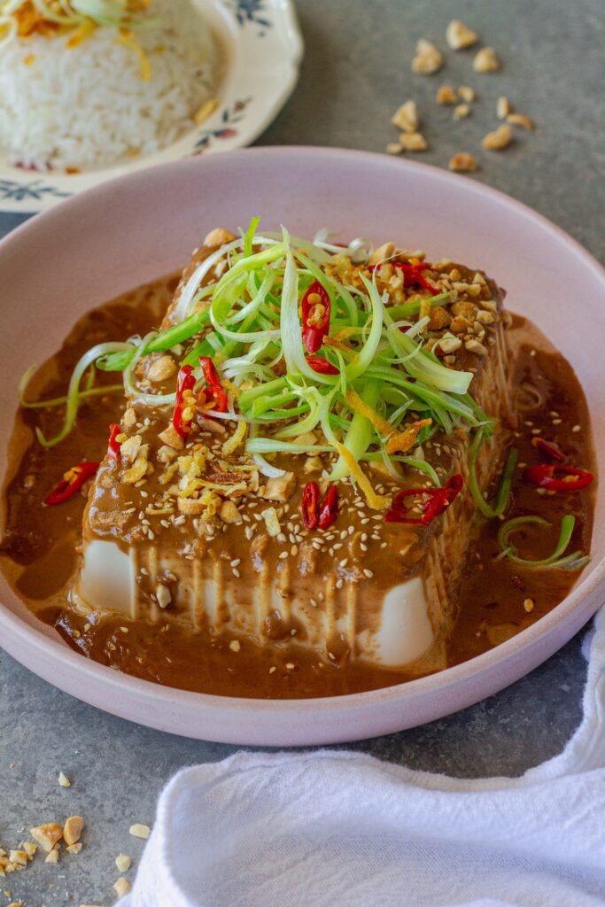 Silken tofu with spicy sesame sauce, topped with green onions, sesame seeds, and crushed peanuts