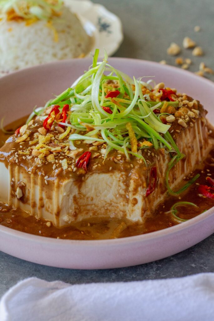 Silken tofu with spicy sesame sauce, topped with green onions, sesame seeds, and crushed peanuts