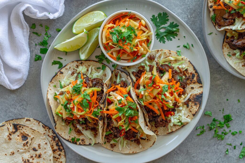 Hoisin-Braised Mushroom and Tofu Tacos topped with fresh slaw and cilantro in warm tortillas