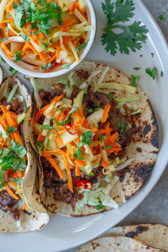 Hoisin-Braised Mushroom and Tofu Tacos topped with fresh slaw and cilantro in warm tortillas