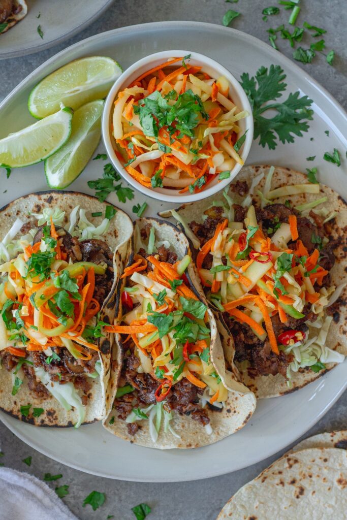 Hoisin-Braised Mushroom and Tofu Tacos topped with fresh slaw and cilantro in warm tortillas