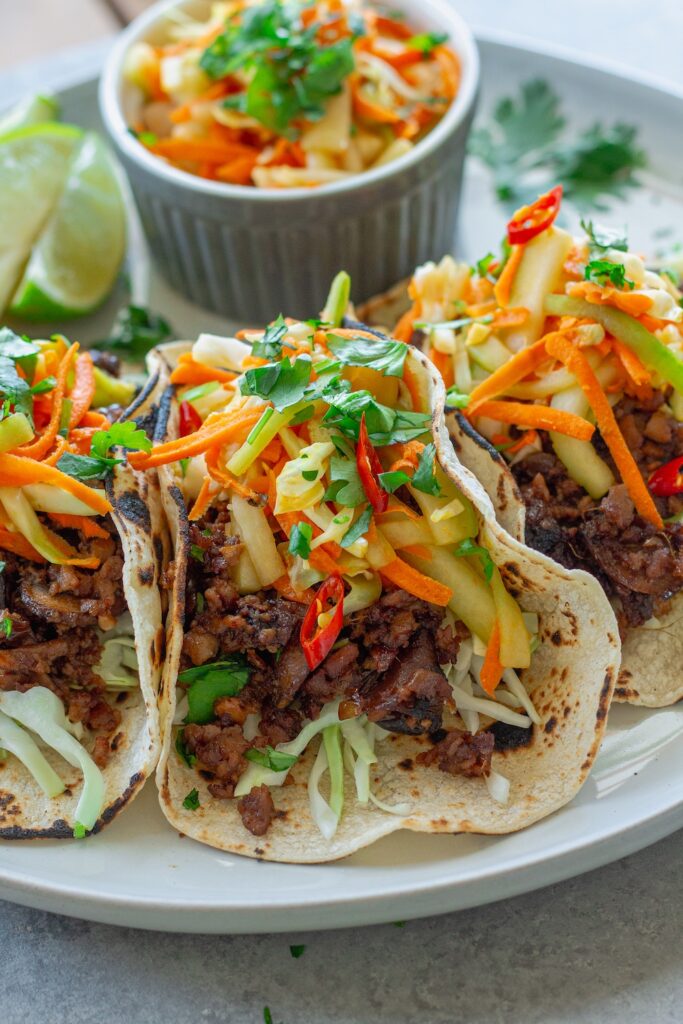 Hoisin-Braised Mushroom and Tofu Tacos topped with fresh slaw and cilantro in warm tortillas