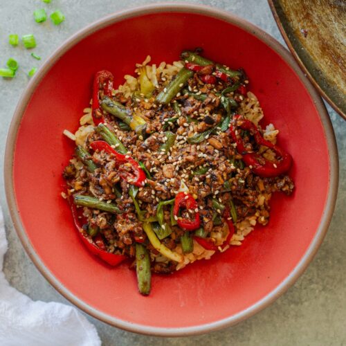 Mongolian tofu stir-fry with crispy grated tofu, green beans, and red chilies served over steamed rice with toasted sesame seeds garnish